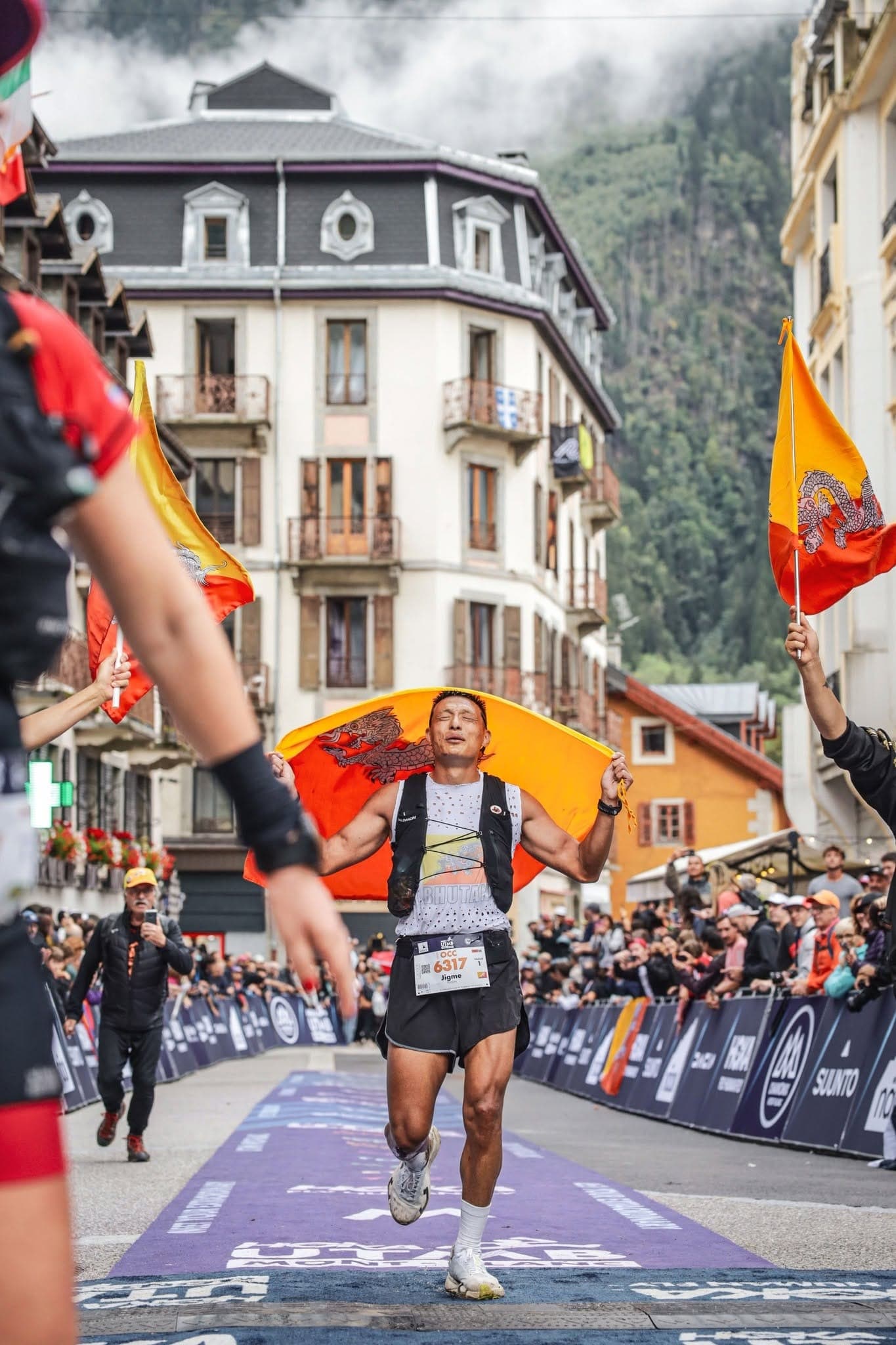 A Bhutanese trail runner draped in the national flag celebrates finishing a mountain ultramarathon